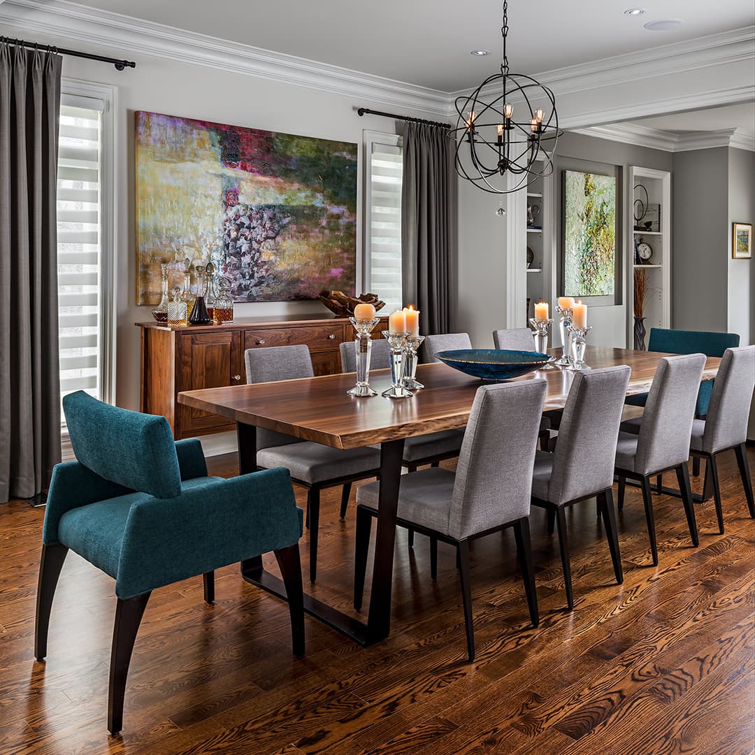 A formal dining room features a large live edge wood table. Teal armchairs sit at the ends. Grey upholstered chairs line the sides. A dark wood buffet sits against a grey wall.