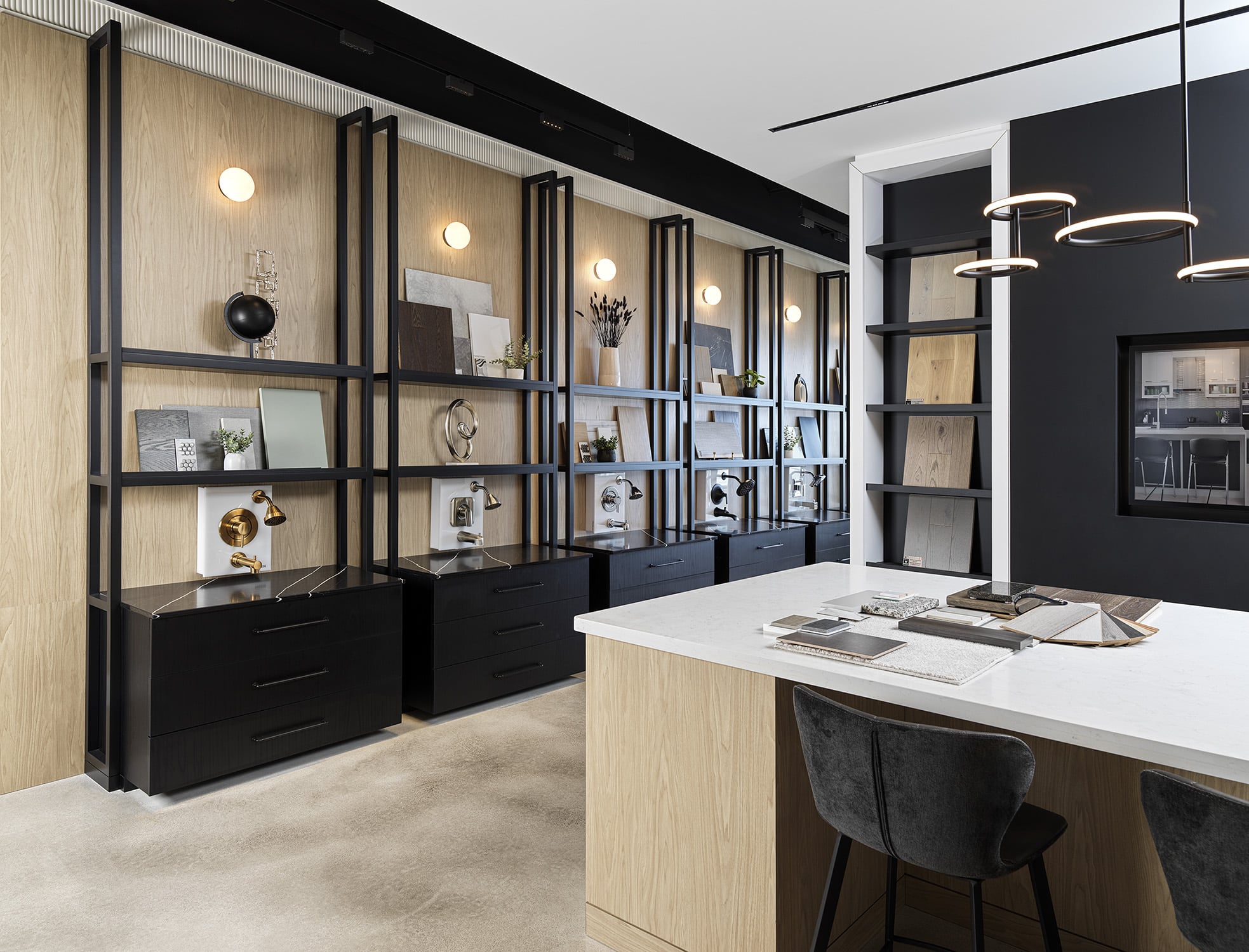 Décor selection area featuring a central sample table, open shelving, blonde woods, curved lighting, and curated finish displays for homebuyers