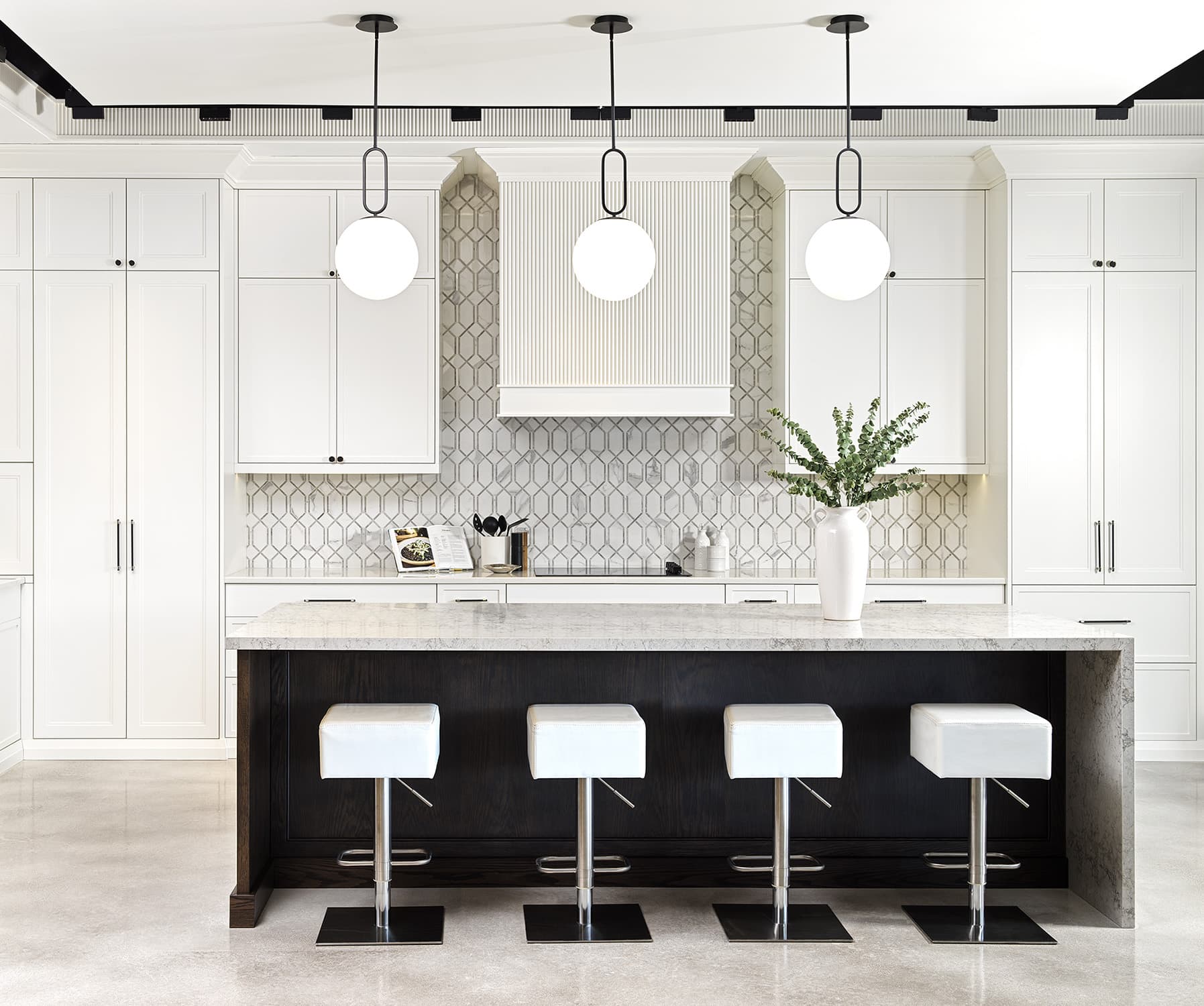 Modern kitchen vignette at Primont XC featuring white shaker cabinetry, stone island with bar stools, and geometric backsplash