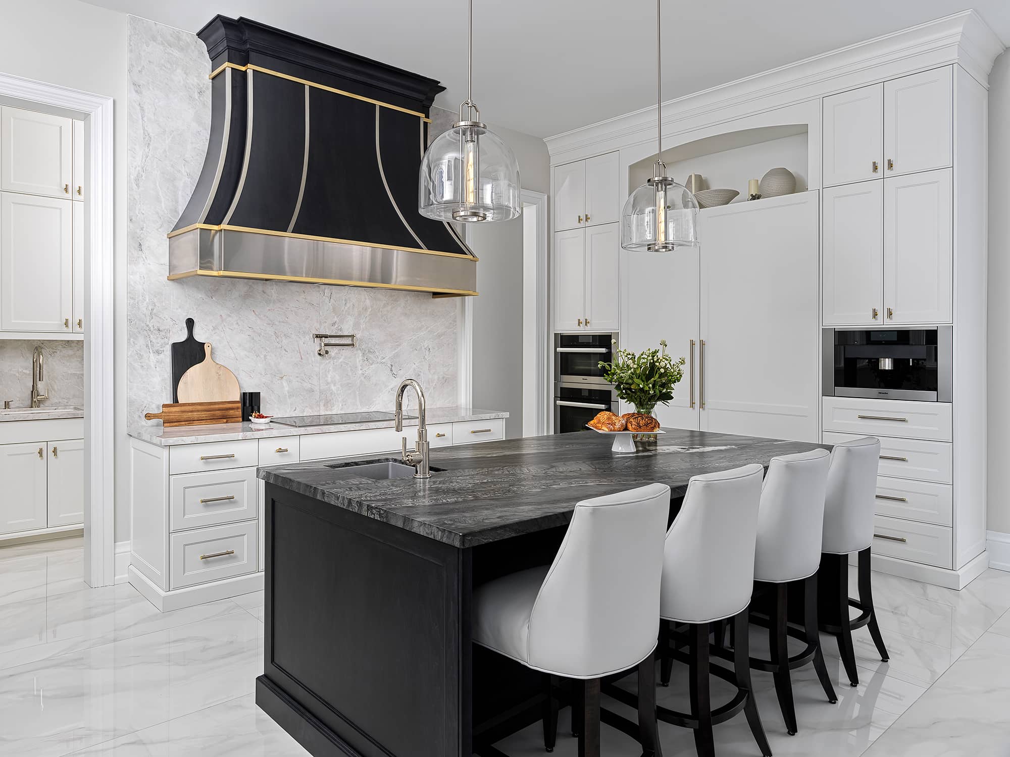 Luxury contemporary kitchen with black and gold range hood, dark island countertop, white cabinetry, and pendant lighting.