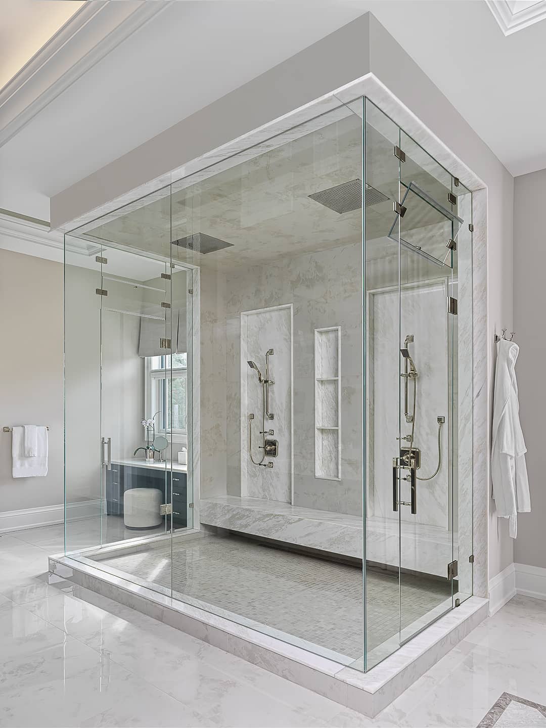 Luxury ensuite bathroom with glass-enclosed steam shower, dual rain showerheads, marble tile walls, and built-in seating.