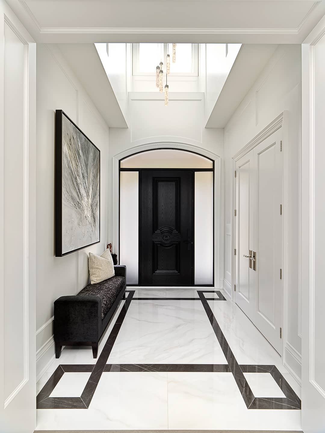 Elegant contemporary foyer with custom marble inlay tile floor, black front door, modern bench, and statement artwork.