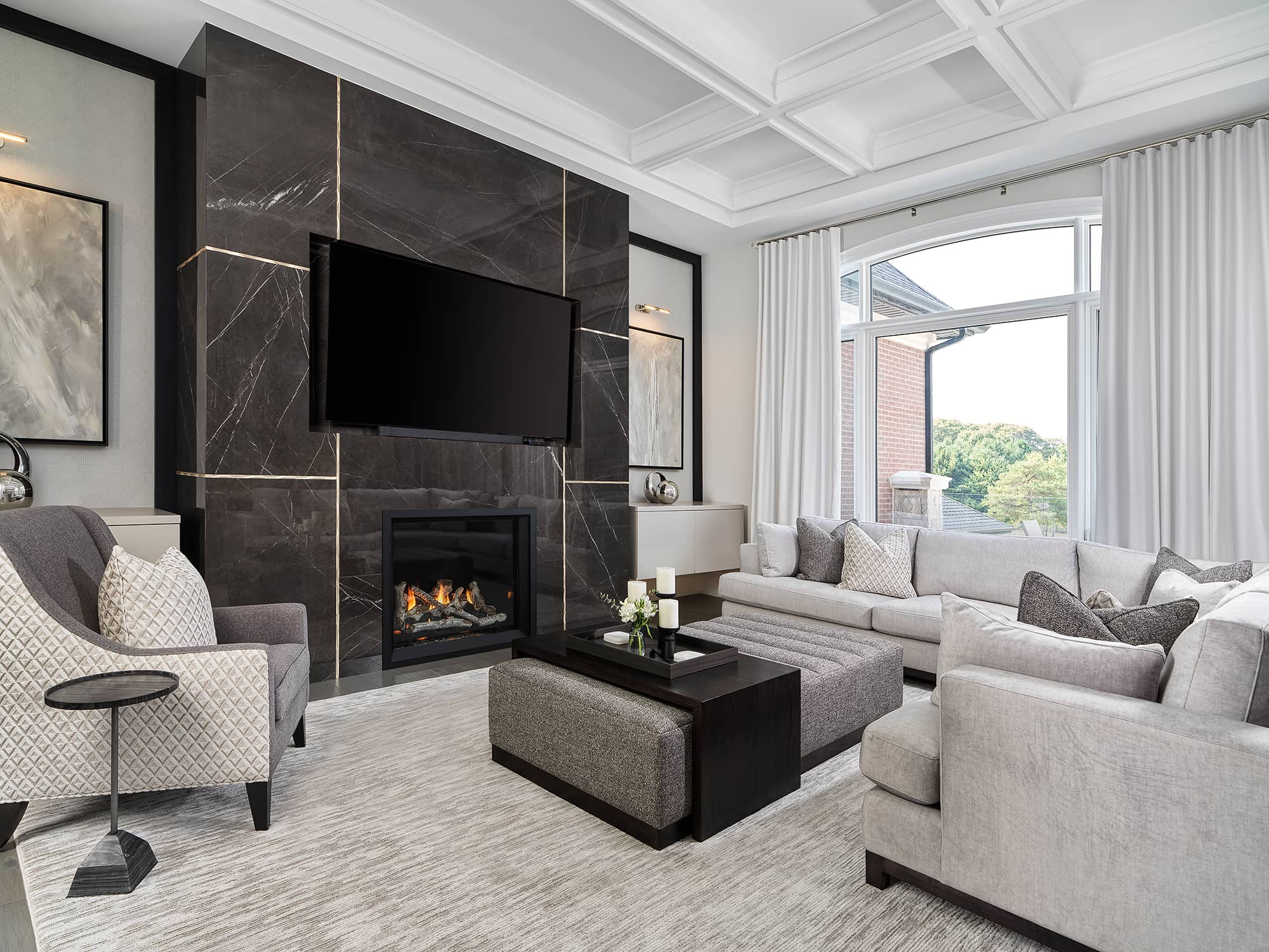 Contemporary great room with marble fireplace wall, coffered ceiling, sectional sofa, and neutral tones accented by modern artwork.