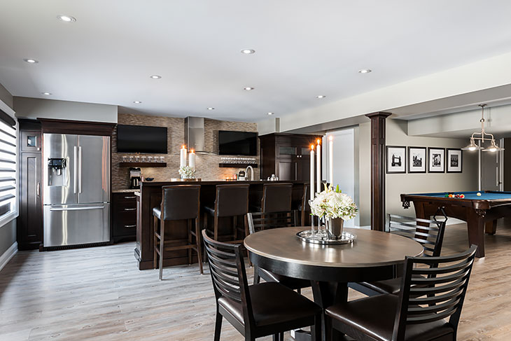 Stylish basement with a modern bar and kitchen area, round dining table, and a pool table in an open-concept entertainment space