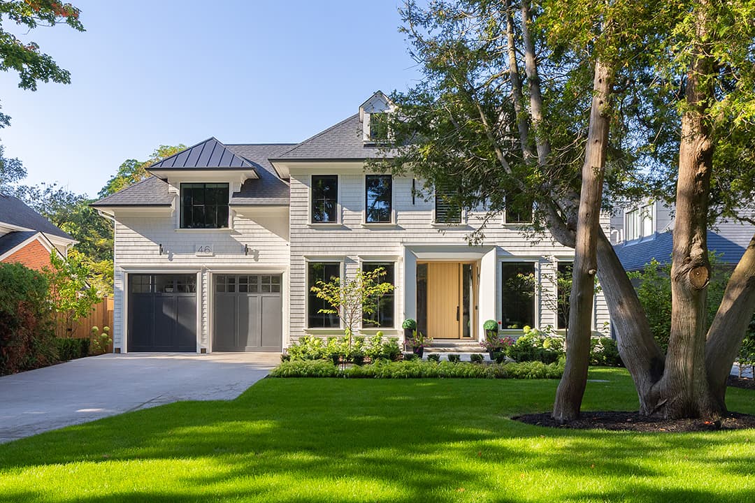 Modern colonial home exterior with light gray siding, black-framed windows, natural wood front door, landscaped front yard, and attached garage.