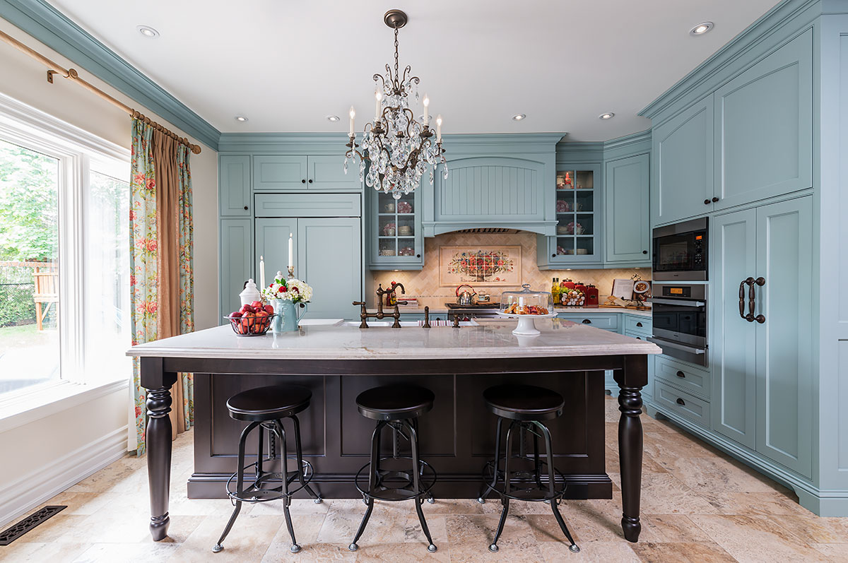 Traditional kitchen with soft blue cabinetry, a large dark wood island, crystal chandelier, and floral accents throughout the space
