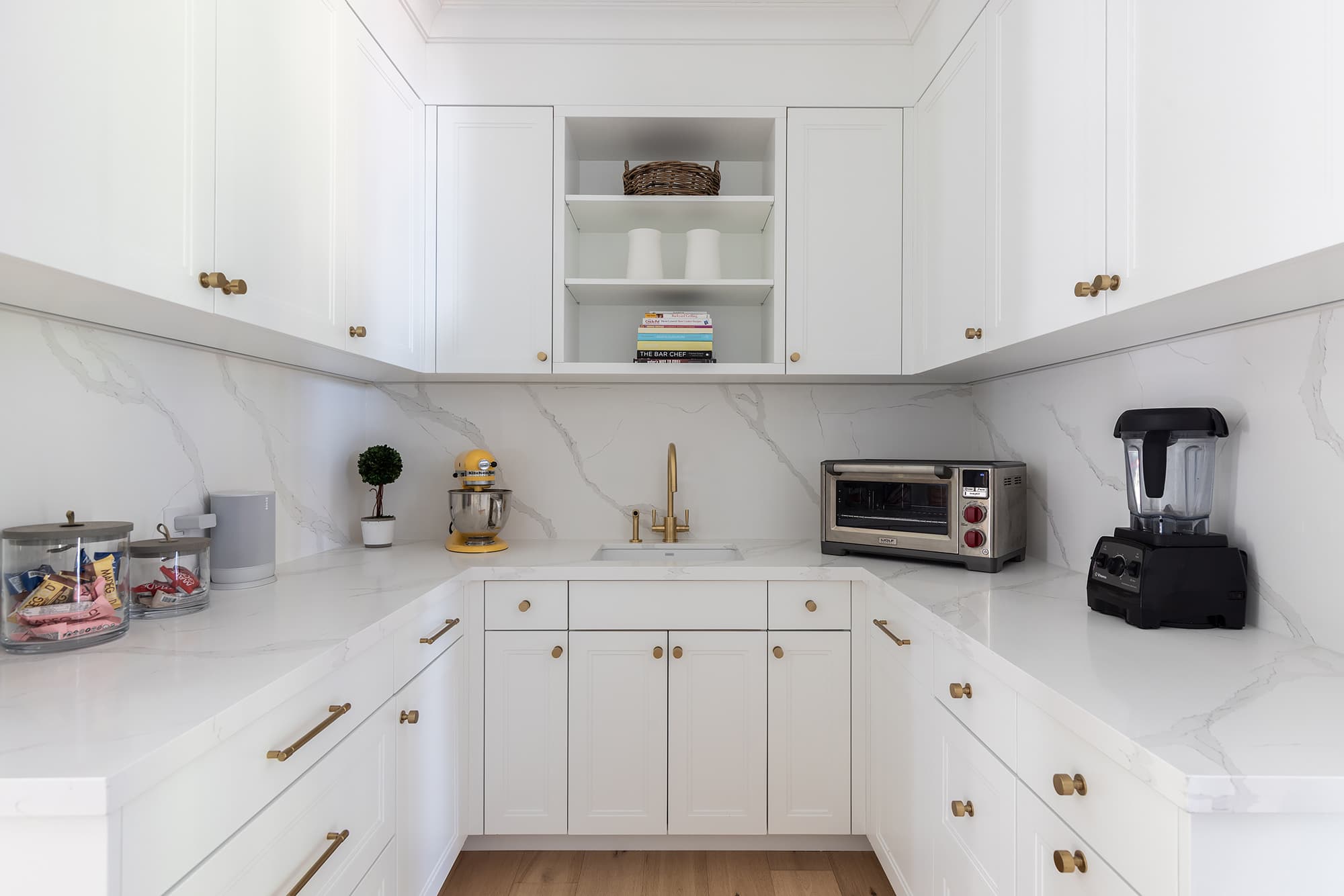 kitchen pantry with white cabinetry, marble countertops and backsplash, brass hardware, open shelving, and integrated prep sink