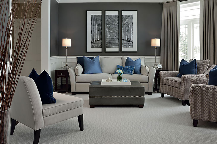 Sophisticated living room with grey walls, neutral seating, blue accent pillows, patterned armchairs, and a large ottoman coffee table