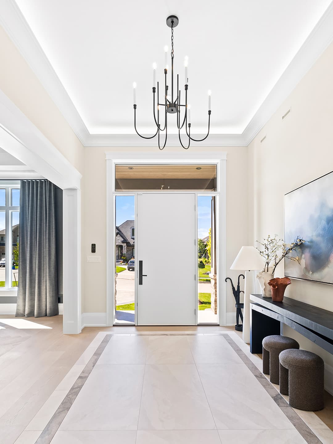 Modern transitional foyer with a statement chandelier, oversized front door, stone tile flooring, and a refined console vignette filled with natural light.