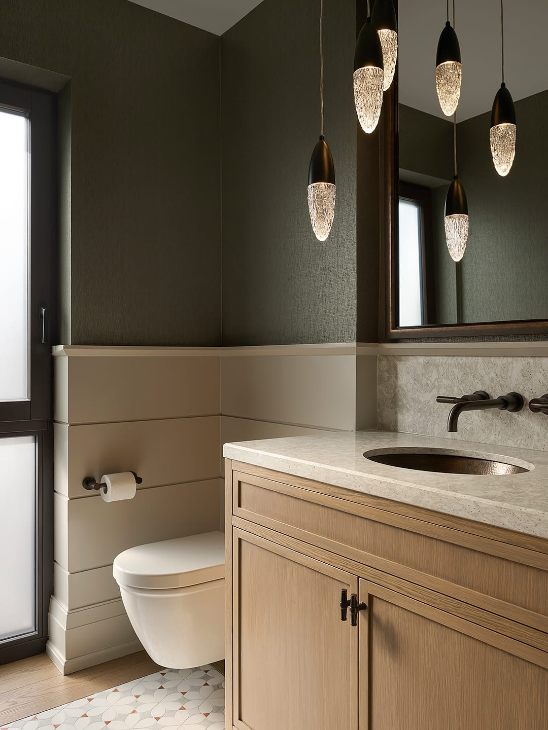 Luxury powder room featuring a light oak vanity with a stone countertop and copper sink, accented by olive green textured wallpaper, cream shiplap wainscoting, and crystalline teardrop pendant lights