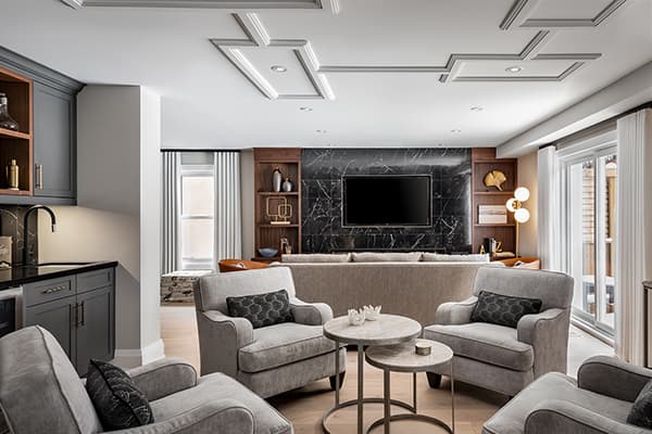 Modern living space with grey armchairs, marble feature wall with a mounted TV, built-in shelving, and large windows bringing in natural light
