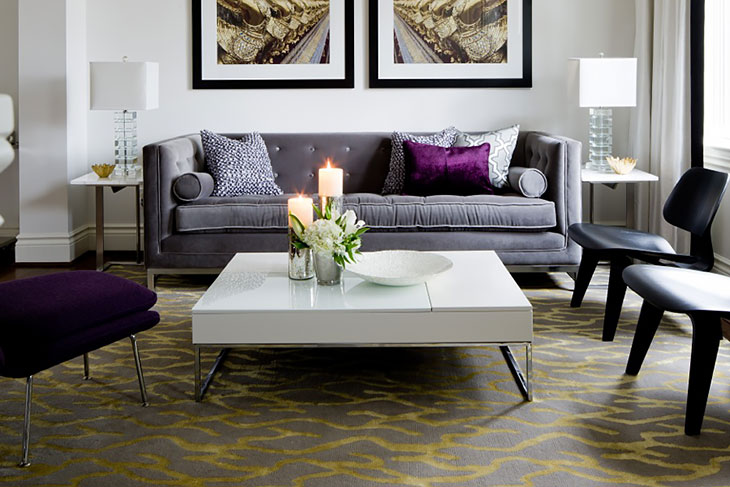 Contemporary living room with a grey tufted sofa, purple accent pillows, modern chairs, and a white low-profile coffee table on a patterned rug