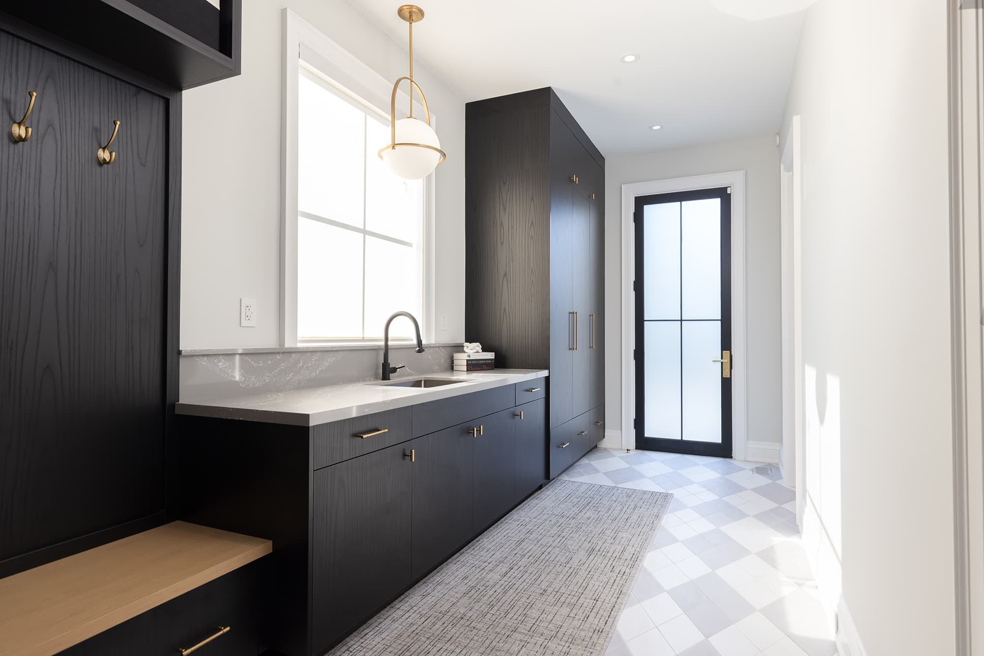 mudroom with black cabinetry, built-in storage, quartz countertop, brass pendant light, patterned tile floor, and glass-paneled exterior door