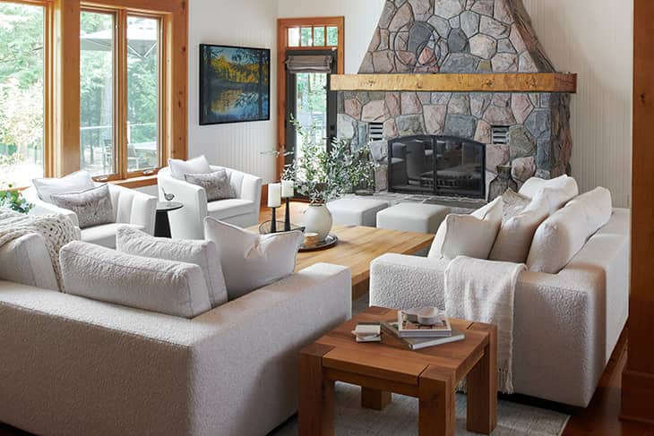 Cozy cottage living room with white textured sofas, natural wood furniture, and a large stone fireplace as the focal point.