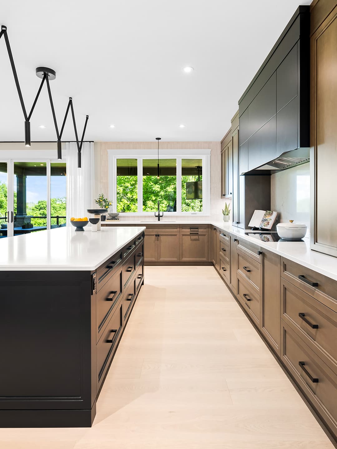 Modern traditional kitchen with two-tone wood and black cabinetry, a large island, integrated appliances, and natural light from large windows.