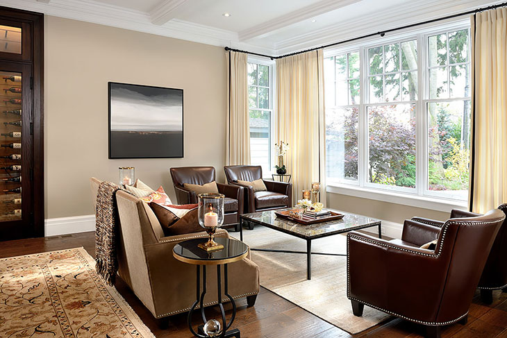 Warm contemporary living room with leather armchairs, a neutral sofa, large windows with cream drapery, and a marble-top coffee table