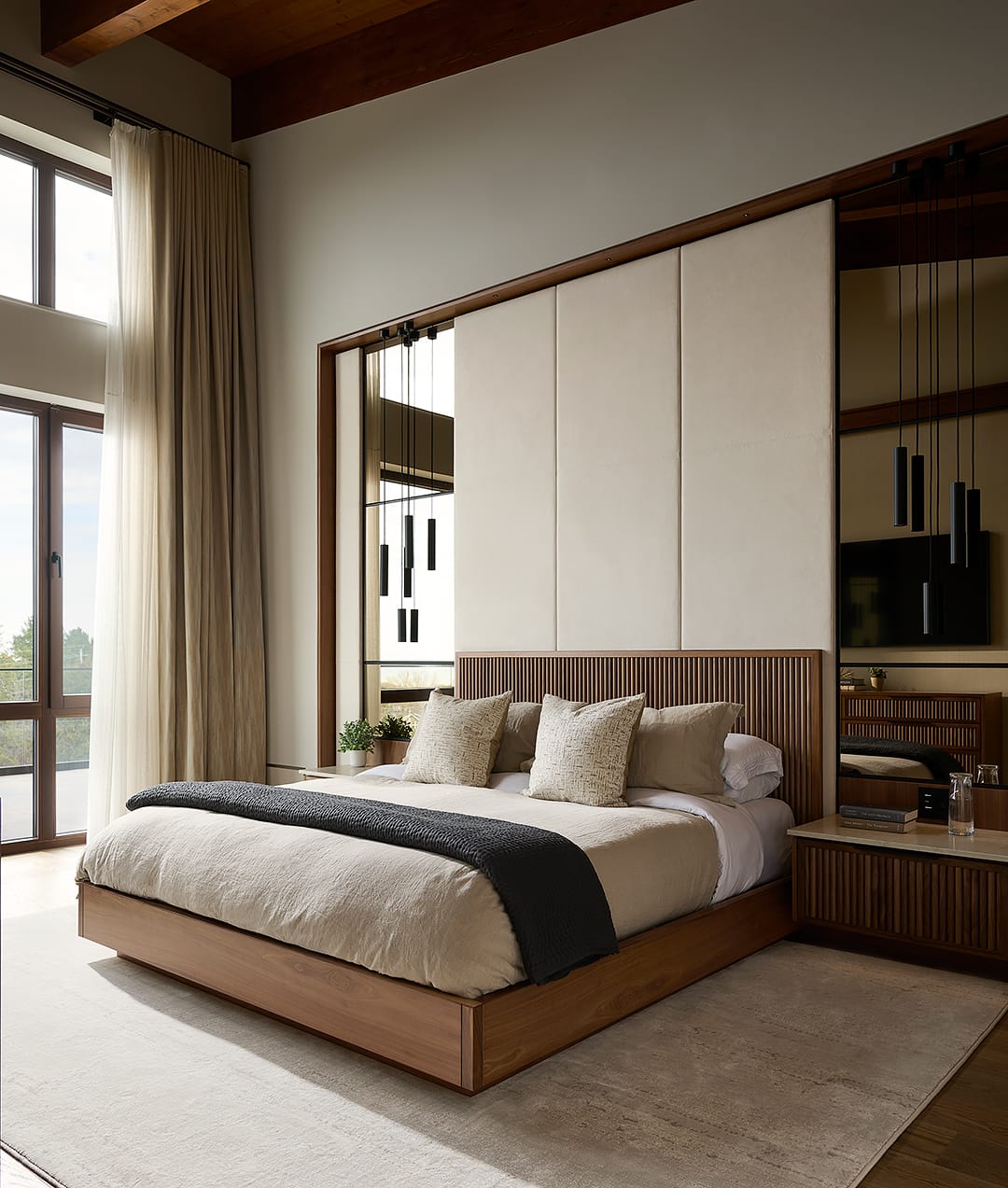 Modern luxury primary bedroom featuring a custom fluted wood bed frame with a floor-to-ceiling upholstered wall panel and integrated mirror accents in a modern alpine chalet