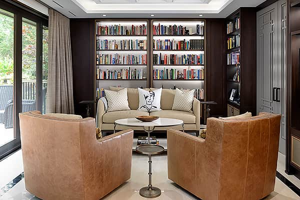 Elegant home library with leather armchairs, built-in bookshelves, neutral sofa, and large sliding doors overlooking the backyard