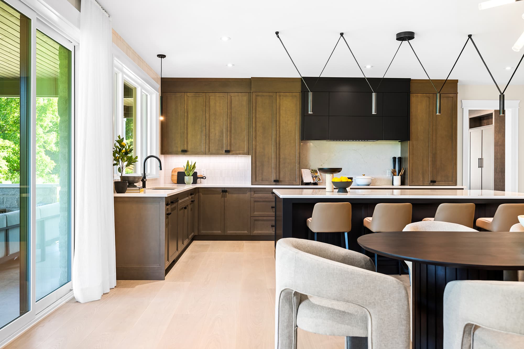 Kitchen with two-tone wood and black cabinetry, a large island with bar seating, integrated pantry storage, and soft natural light.