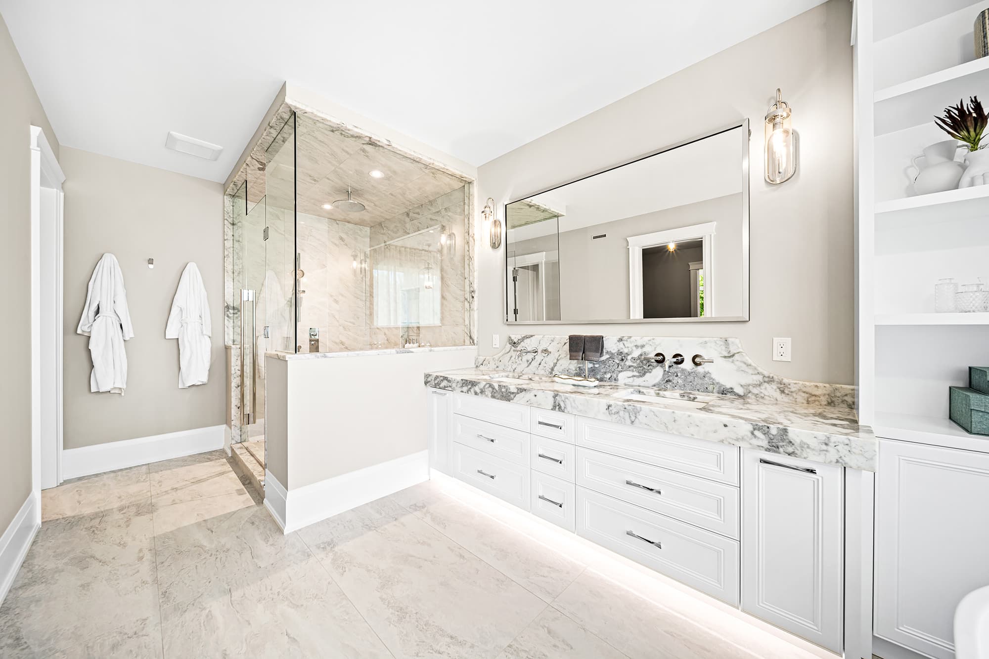 Primary bathroom with a marble walk-in shower, custom white vanity, wall-mounted faucets, and soft neutral finishes.