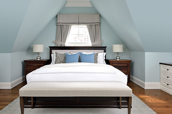 Calm attic bedroom with sloped ceilings, a dark wood bed, soft blue walls, and a bench at the foot of the bed