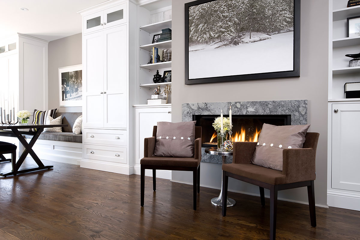 Cozy living area with a modern fireplace, brown accent chairs, built-in white cabinetry, and a winter landscape artwork above the mantel
