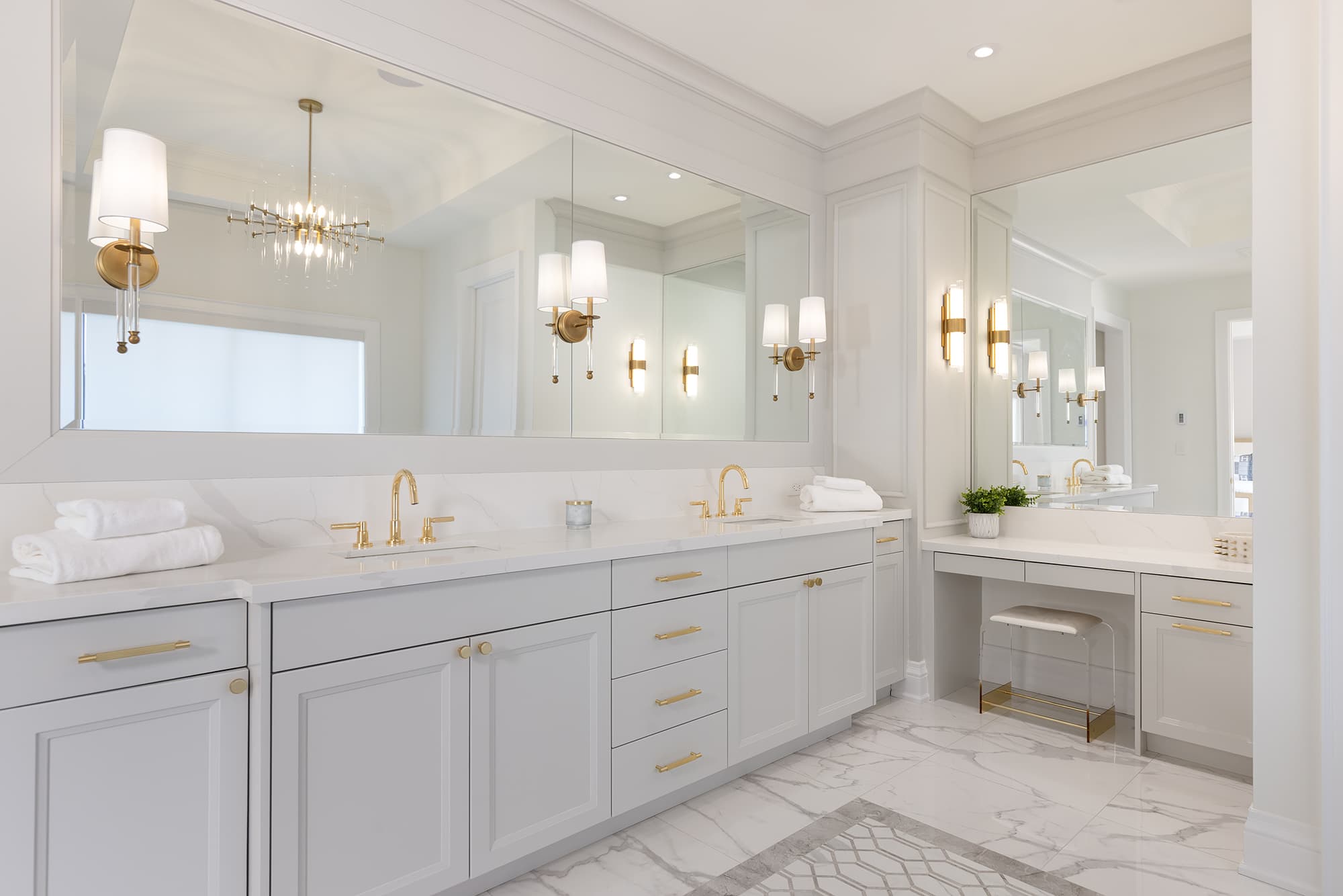 primary bathroom with double vanity, light gray cabinetry, marble countertops and floors, brass fixtures, and large wall mirrors.